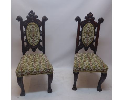 A pair of 19th Century mahogany hall chairs with carved lion head finials, armorial tapestry upholstery and raised on sabre l