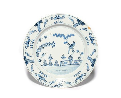 A large delftware dish or charger, c.1740, painted in blue with a bird perched on a branch beside an ornamental fence, the ri