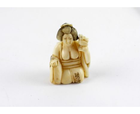 An early 20th century Japanese ivory netsuke in the form of a partially-clad young woman holding a bird, red character mark t