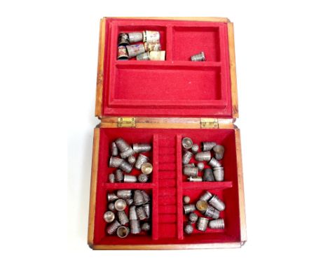 A vintage walnut box containing over forty hallmarked silver thimbles and a quantity of cloisonné and other thimbles.