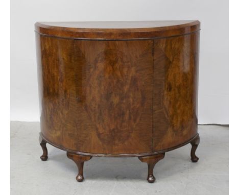 An early/mid-20th century walnut demi-lune cabinet, the caddy top surmounting a single arched door flanked by panels supporte