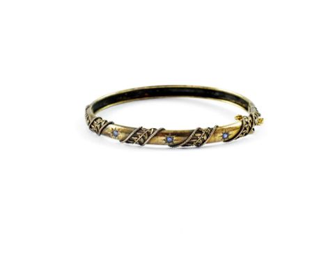 An Edwardian yellow metal bangle, star-set with small blue stones and leaf decoration, approx 9.5g.