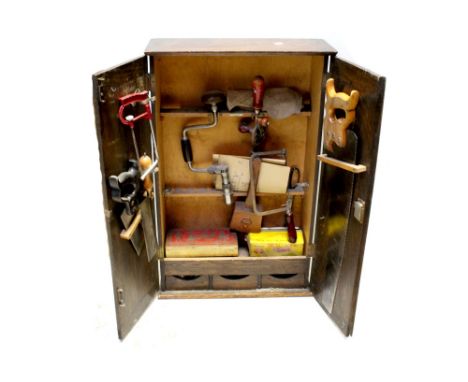 A stained pine joiner's cabinet containing a number of vintage tools to include saw, screwdrivers, bit and brace, drills, var