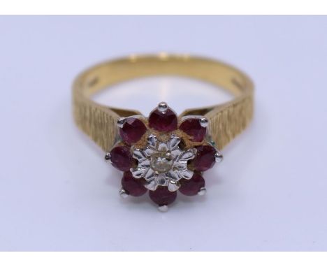 An 18ct gold, ruby and diamond ring, illusion set central single cut diamond bordered by eight round cut rubies, with texture