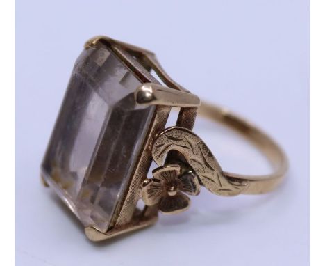 A 9ct. yellow gold and topaz cocktail ring, four claw set mixed rectangular cut topaz with textured gallery and flower and le