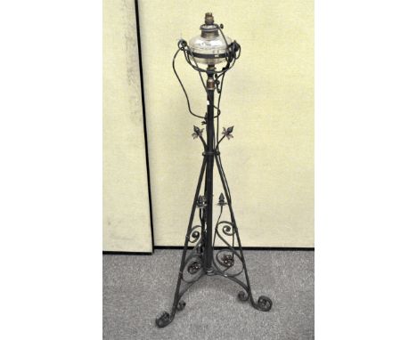 A wrought iron standard lamp featuring a tripod stand with floral and scroll motifs, adapted to electricity, height 137 cm
