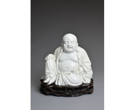 A CHINESE BLANC DE CHINE FIGURE OF BUDAI, QING DYNASTY. The figure seated dressed in robes open at the chest, with his right 