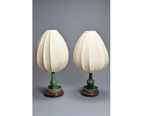 TWO CHINESE GREEN GLAZED CERAMIC CONVERTED CANDLESTICK LAMPS. Each candlestick with drip tray mounted on a wooden base, with 