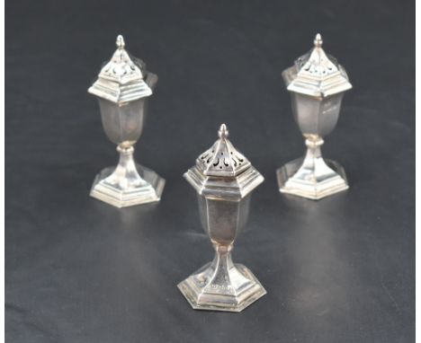 A group of three silver pepperettes, of hexagonal form with pierced finial topped pull-off covers, on short stems and spreadi