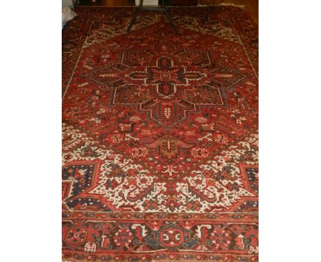 A red ground Heriz carpet, decorated with stylised flower head medallions to centre on a geometric patterned ground, within m