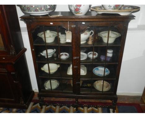 An oak cabinet bookcase, having a pair of astragal panel doors enclosing shelves, on short square and turned legs, W. 115cm.