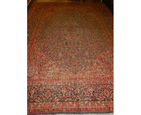 A large red ground Kerman carpet, decorated with scrolling foliage to centre, within floral borders, fringed, L. 340cm, W.270