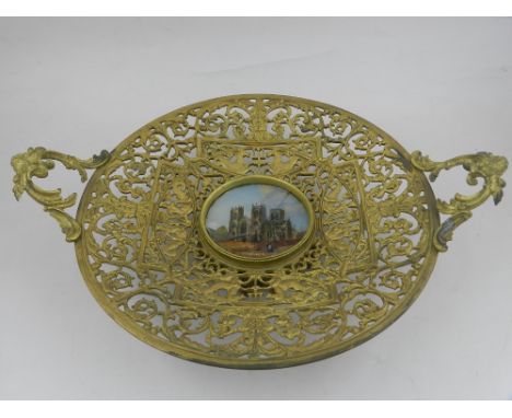 A brass twin handled tazza, with glazed panel to centre, painted with York Minster, the pierced frame having scrolling foliag