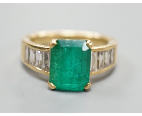 A modern yellow metal and single stone emerald set dress ring, with graduated baguette cut diamond set shoulders, size M/N, g