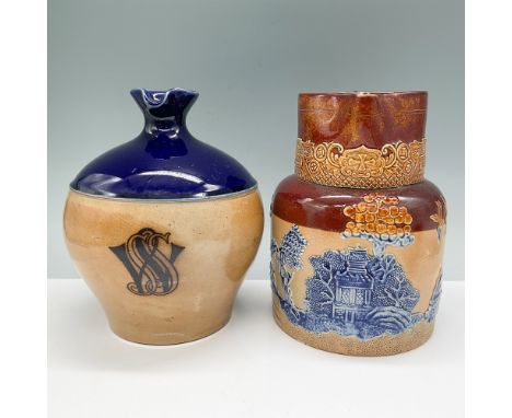 A pair of Doulton Lambeth stoneware jugs featuring intricate relief designs. The first jug, with a cobalt blue glaze and mono