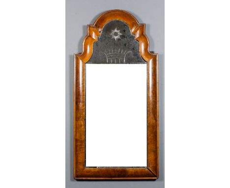 A walnut wall mirror of early 18th Century design, the deep rectangular cushion frame with arcaded top, inset with a plain be