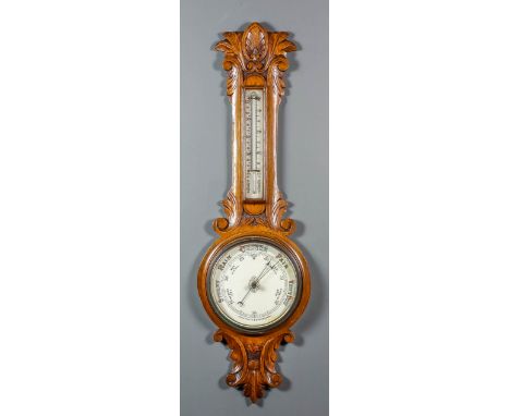 A late Victorian oak cased aneroid barometer and thermometer, the 7.25ins diameter white dial, in wheel pattern case, carved 