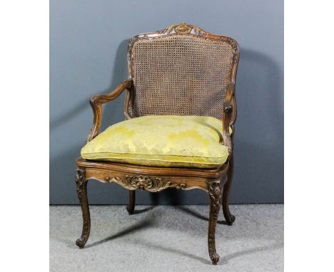 A French walnut and parcel gilt framed open arm fauteuil, the shaped and moulded back with scroll and leaf cresting, moulded 