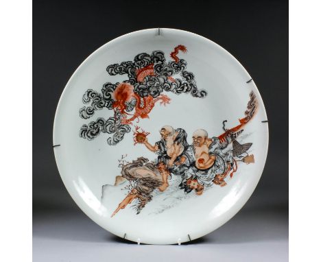 A Japanese porcelain charger enamelled in black, orange and red with a five clawed dragon above two seated figures with a tig