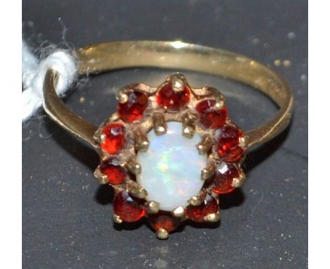 An opal and garnet cluster ring, central oval opal, flashing green,red and blue colour play, surrounded by a band of ten red 