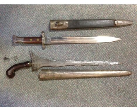 A late 19th century Malayan Kris, the shaped blade with partially carved hardwood handle within a white metal scabbard (tests