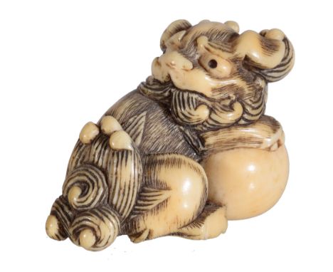 Ω A Japanese Ivory Netsuke, carved in the form of a seated Shishi, its forepaws on a large ball, its head turned back over it