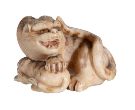 Ω A Japanese Ivory Netsuke, carved as a Siberian Tiger and its cub, the mother's head turned back and snarling as she rests a