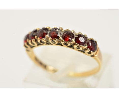 A 9CT GOLD GARNET RING, set with a row of seven circular cut to the plain polished band, with 9ct hallmark for London, ring s