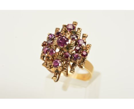 A GARNET DRESS RING, a tiered ring with open metal work set with fifteen circular garnets upon a plain polished band, stamped
