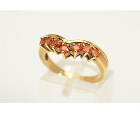A 9CT GOLD GEM RING, the V-shape front set with a line of seven circular orange gems assessed as hessonite garnets, with 9ct 