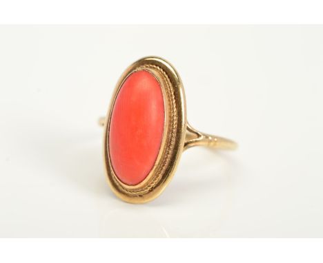 A 9CT GOLD CORAL RING, designed as an elongated oval coral cabochon within a collet setting and rope twist surround to the bi