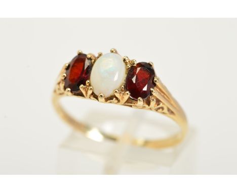 A 9CT OPAL AND RUBY RING, designed with a central oval opal cabochon flanked either side with an oval cut garnet, within shar