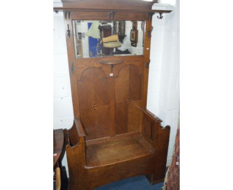 AN ARTS AND CRAFTS STYLE OAK HALL STAND/SEAT, with a rectangular bevelled mirror, various coat hooks, hinged storage flanked 