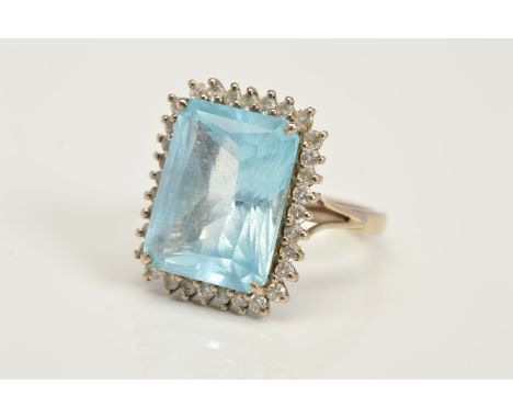 AN 18CT WHITE GOLD TOPAZ AND DIAMOND CLUSTER RING, designed as a rectangular blue topaz within a four claw setting and brilli