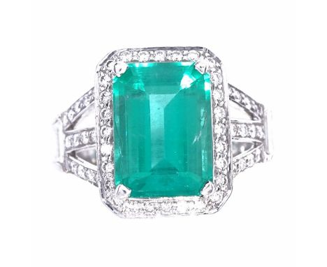 A rectangular emerald and diamond cluster ring, central large emerald step-cut emerald approx 3.88ct, surrounded by round bri