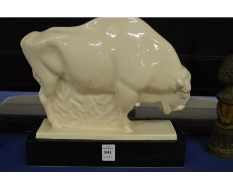 A stylised white pottery model of a bison on a wooden base.