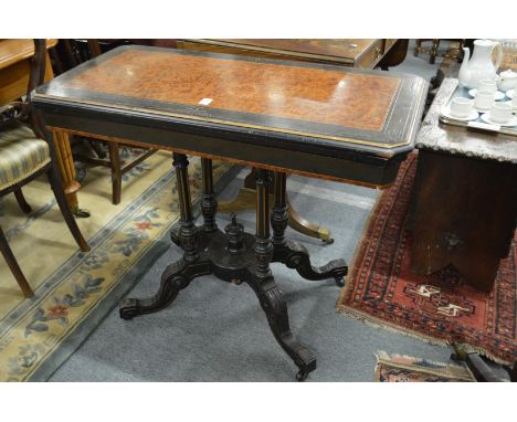 A Victorian burr wood and ebonised fold over card table on column support with splay legs.