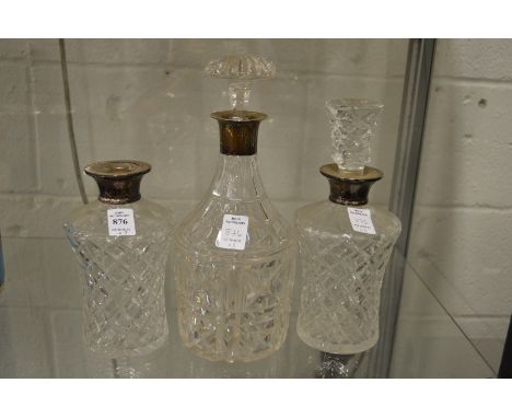 A pair of cut glass decanters with silver collars and a similar decanter (lacking one stopper).