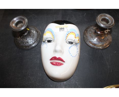 A pair of silver coloured candlesticks and a decorative ceramic mask  