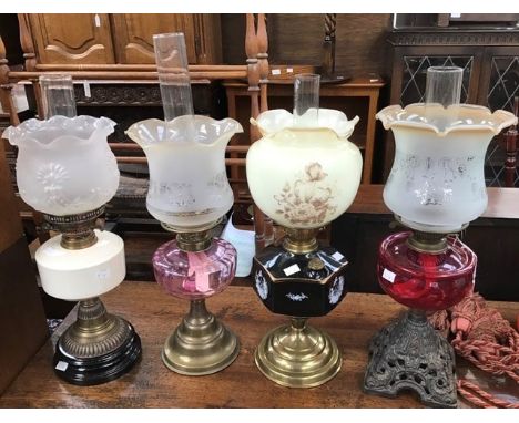 Four late 19th Century oil lamps with shades and funnels, ruby glass body example and ceramic example