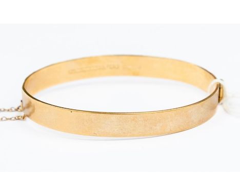 A 9ct gold bangle, hinged with engraved leaf decoration, width approx. 7mm, internal diameter approx. 60mm, safety chain,  we