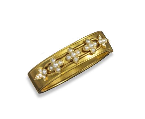 A Victorian gold bangle, decorated with seed pearl flower head clusters, in 18ct yellow gold.