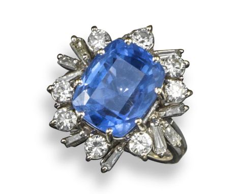 A sapphire and diamond cluster ring, the cushion-shaped pale blue sapphire is set within a surround of circular and tapered b