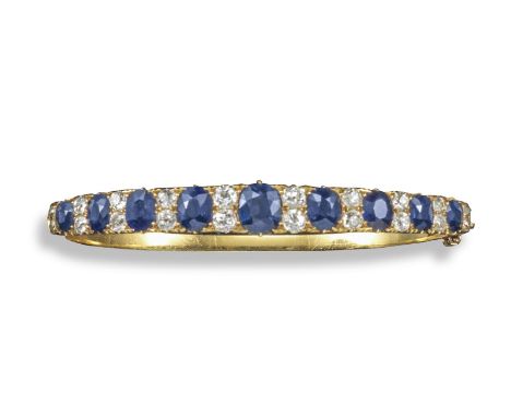 A Victorian sapphire and diamond set gold hinged bangle, set with a line of graduated oval-shaped sapphires, each spaced with