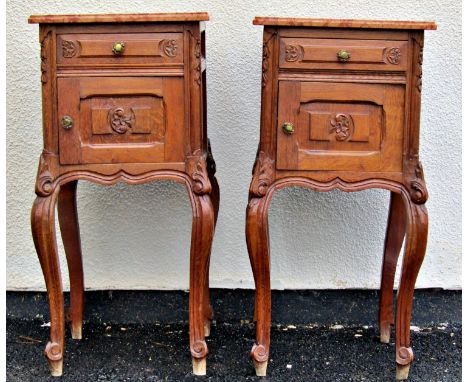 A pair of carved oak bedside/lamp tables each with polished marble tops over a frieze drawer and cupboard raised on cabriole 