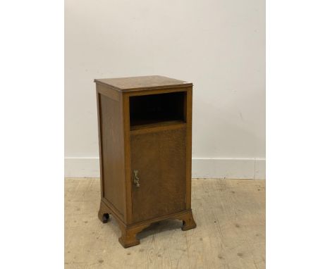 An early 20th century oak bedside cupboard, with open shelf above a single door enclosing a shelf, raised on splayed bracket 