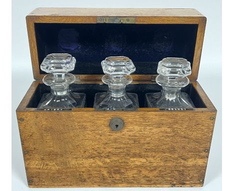 An early twentieth century leather lined oak spirits container/tantalus with three clear glass decanters for Whisky, Gin, and