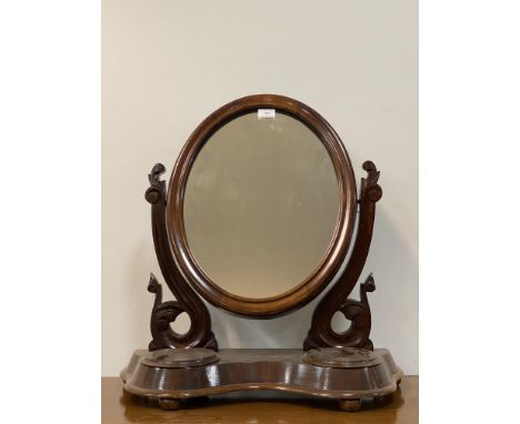 A Victorian mahogany vanity mirror, the oval mirror swivelling between two floral carved uprights, above two trinket recesses