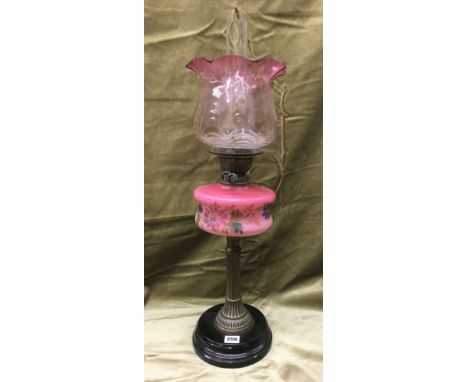 19TH CENTURY OIL LAMP WITH A FLUTED METAL COLUMN AND A FLORAL PAINTED RESERVOIR WITH CRANBERRY TINTED GLASS SHADE WITH CRIMPE