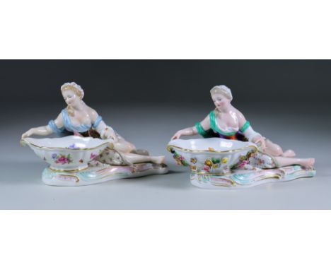 Two Meissen Porcelain Salts, modelled as reclining female figures holding dishes of shaped outline, Model No. 2975, with cros